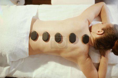 Healthcare time. relaxed modern woman in massage cabinet having hot stone massage and laying on massage table.