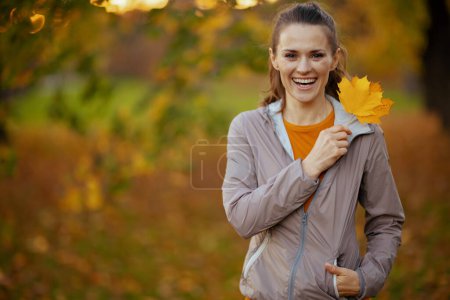 Photo for Hello autumn. Portrait of happy elegant female in fitness clothes in the park with autumn leaf. - Royalty Free Image