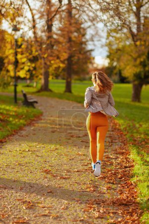 Téléchargez les photos : Bonjour l'automne. Vu de derrière femme en vêtements de fitness dans le parc jogging. - en image libre de droit