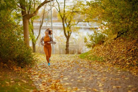 Photo for Hello autumn. Full length portrait of 40 years old woman in fitness clothes in the park jogging. - Royalty Free Image