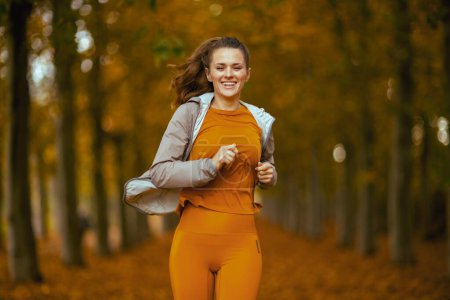 Téléchargez les photos : Bonjour l'automne. heureux à la mode 40 ans femme en vêtements de fitness dans le parc en cours d'exécution. - en image libre de droit