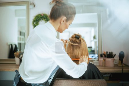 Téléchargez les photos : Vu de derrière femme coiffeuse dans un studio de coiffure moderne avec brosse à cheveux et client. - en image libre de droit