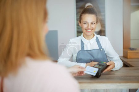 Photo for Woman hairdresser in modern beauty studio with client accepting credit card payments via terminal on reception. - Royalty Free Image