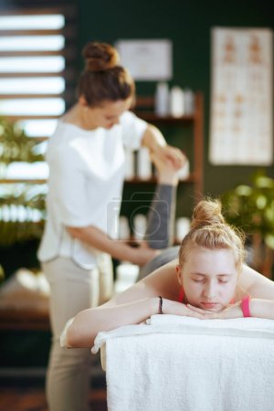 Photo for Healthcare time. massage therapist woman in massage cabinet with teenage client making massage on massage table. - Royalty Free Image