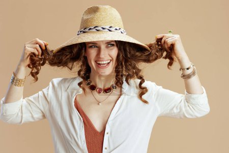 Photo for Beach vacation. smiling elegant 40 years old woman in white blouse and shorts isolated on beige with summer hat. - Royalty Free Image