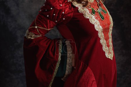 Téléchargez les photos : Gros plan sur la reine médiévale en robe rouge ayant mal au dos sur fond gris foncé. - en image libre de droit