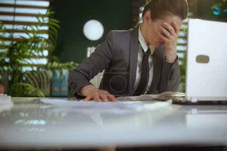 Un nuevo trabajo. mujer trabajadora moderna infeliz en la oficina verde moderna en traje de negocios gris con el ordenador portátil tirar documentos.