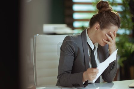 Un nuevo trabajo. infeliz moderno 40 años de edad, mujer trabajadora en moderna oficina verde en traje de negocios gris con carta de despido de los empleados.