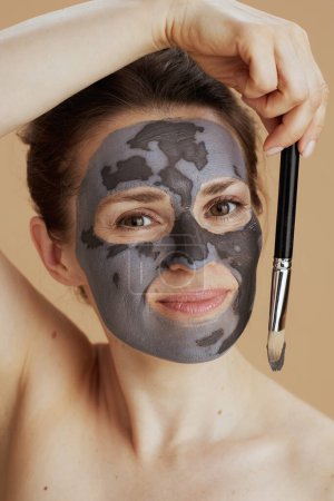 Foto de Joven mujer de 40 años con cepillo y máscara cosmética contra fondo beige. - Imagen libre de derechos