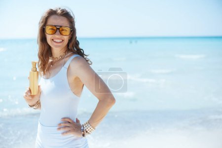 sonriente mujer moderna en la orilla del mar con spf.
