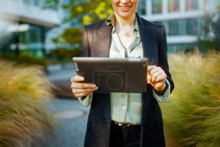 Closeup on middle aged business woman in business district in black jacket using digital tablet.