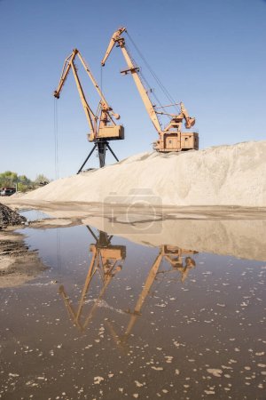 Foto de Grúas industriales portuarias en el depósito de descarga de arena de río en un día claro y soleado - Imagen libre de derechos