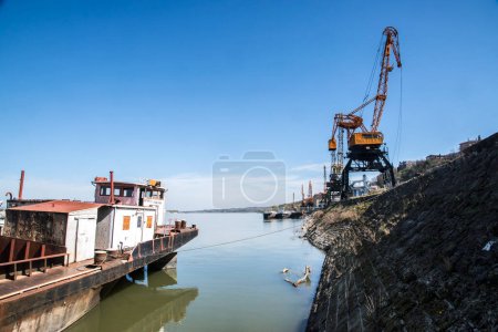 Barcaza de carga fluvial a granel y grúas industriales en puerto fluvial en día soleado