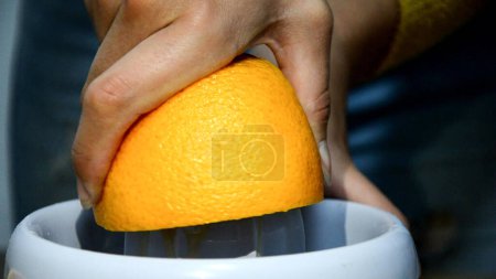 Photo for Woman hand juicing fresh orange fruit on juicer HD video. Preparing citrus juice drink at home kitchen. Squeezing on squeezer, reverse video - Royalty Free Image