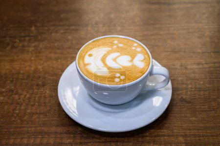 A white cup of latte with a detailed foam art on a warm wooden background