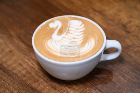 Primer plano de un café con leche bellamente elaborado con un arte de cisne en la parte superior, servido en una taza blanca