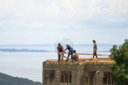 Téléchargez les photos : Bugala Island, Ouganda - 30 mai 2022 : Travailleurs de la construction construisant une maison, debout sur le toit, journée ensoleillée en mai - en image libre de droit