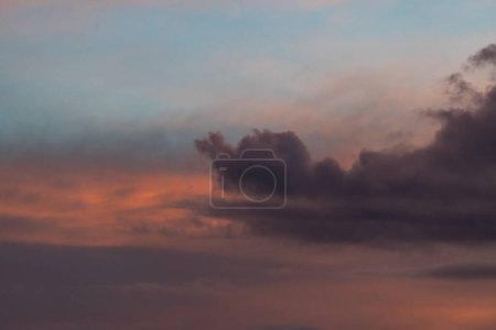 Graue Wolken vor blauem Himmel, manchmal orange, beleuchtet von der untergehenden Sonne.