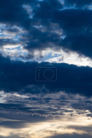 A vertical photograph with contrasting dark gray clouds filling almost the entire blue sky in the photograph