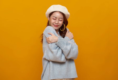 Photo for Beautiful Asian teenager woman hugging and embracing herself isolated on studio yellow background. selflove appreciation and self care concept. - Royalty Free Image