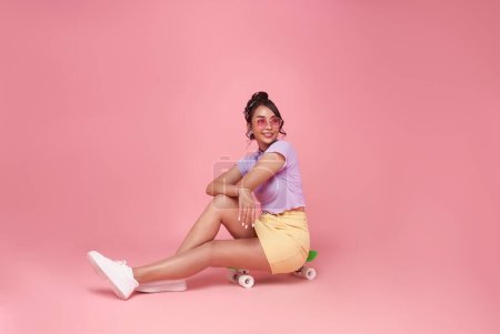 Photo for Full length of cheerful young asian teen woman sitting on skateboard have fun isolated on pink background studio portrait. People lifestyle concept. - Royalty Free Image