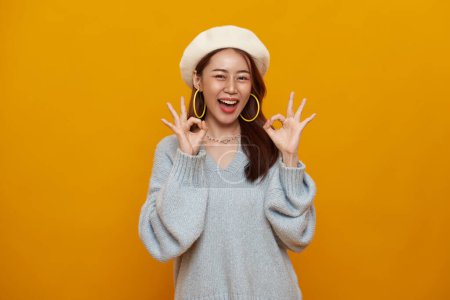 Photo for Happy smiling Asian young woman smiling and showing hand ok sign isolated on yellow background. - Royalty Free Image