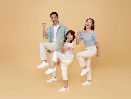 Photo for Full body happy fun Asian family doing winner gesture celebrate clenching fists raise up leg isolated on nude color background. - Royalty Free Image