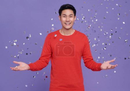 Photo for Young happy satisfied excited fun surprised amazed asian man 20s in casual red clothes tossing throwing confetti isolated on purple background. - Royalty Free Image