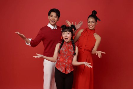 Photo for Happy asian family wearing red costume presenting or showing open hand palm with copy space for product isolated on red background. Present product advertising concept. - Royalty Free Image