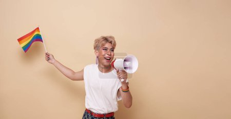 Photo for Happy smiling youth asian transgender LGBT waving hold rainbow flag and megaphone announce equality isolated on nude color background. - Royalty Free Image