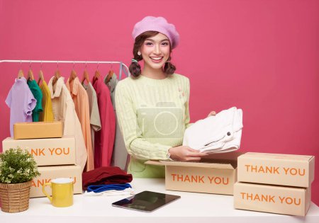 Young asian woman startup small business freelance seller clothing with parcel box and tablet computer on table isolated on pink background, Online marketing and delivery concept
