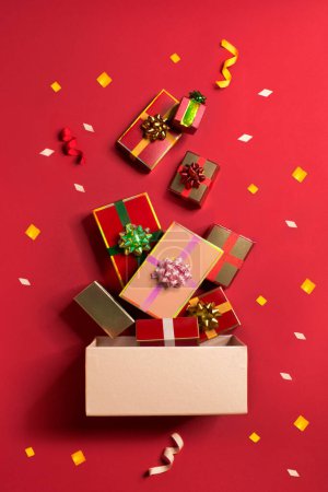Photo pour Red gift boxes coming out from a pink box on red background with confetti. Flat lay still life image. - image libre de droit