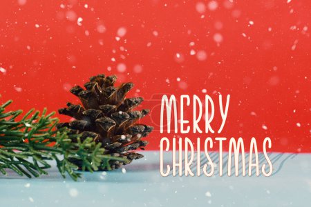 Téléchargez les photos : Greeting card with merry christmas lettering on red background with christmas tree branch and pine cone - en image libre de droit
