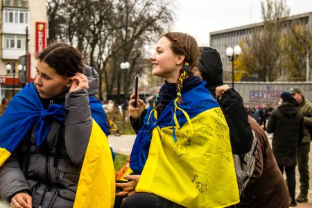 Foto de Algunos ciudadanos de Kherson con la bandera de Ucrania en forma de capa celebran la liberación de la ciudad en la Plaza de la Libertad en el centro de la ciudad. Las tropas rusas dejaron Kherson después de una ocupación de nueve meses y una contraofensiva por parte de los ucranianos. - Imagen libre de derechos