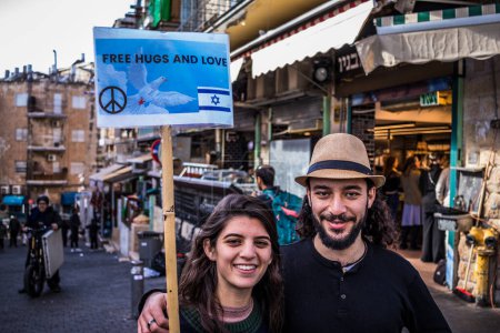 Photo for Jerusalem, Israel - December 22, 2023 A couple of young peace activists offer free hugs at the Mahane Yehuda Market, often called "The Shuk", is a market in Jerusalem. - Royalty Free Image