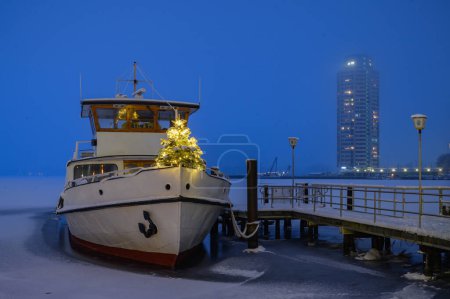 Fähre mit Weihnachtsbaum am Bugrand. Schneebedeckte Schiffsboote liegen im Winter an der Seebrücke in Schleswig. Schleswig-Holstein. Winter, Weihnachten an der Schlei, Schleswig.