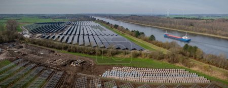 Luftaufnahme der Baustelle eines Photovoltaik-Parks mit Kartons auf Paletten mit Solarmodulen und Komponenten für Sonnenkollektoren und installierten Regalen für Sonnenkollektoren Freiflächen-PV.