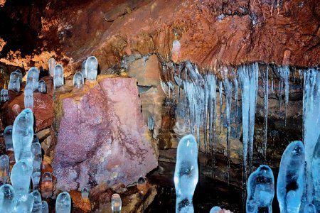 Des formations glaciaires semblables à des stalagmites dans une grotte de lave avec des parois rocheuses texturées, mettant en valeur des phénomènes naturels hivernaux. Lieu : La grotte - Islande.