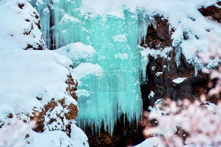 Cascade gelée avec glaçons entourée de rochers enneigés Lieu : Hraunfossar, Islande.