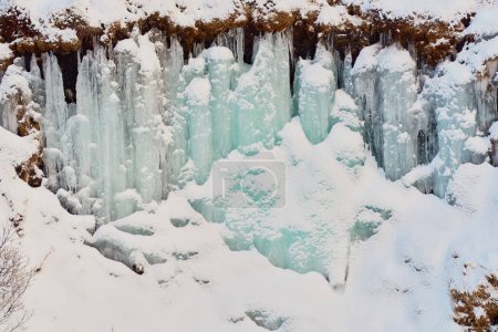 Pays des merveilles hivernales avec cascade gelée et rochers enneigés. Localisation : Hraunfossar, Islande.