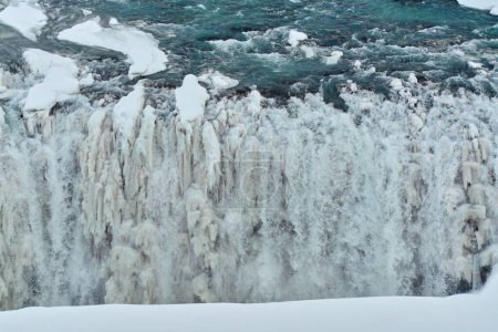 Majestic frozen waterfall with icicles and snow viewed from the side of a cliff. Location: Gullfoss Falls, Iceland.