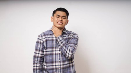 Foto de Joven asiático tocándose la garganta mostrando expresión de dolor sobre fondo blanco. plano de estudio - Imagen libre de derechos