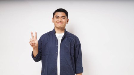 Photo for Young Asian man showing happy face expression while giving two fingers sign - Royalty Free Image