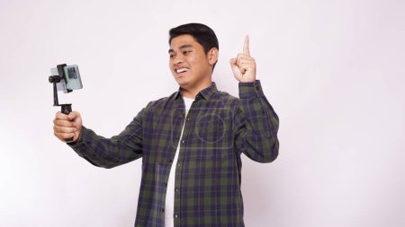 Photo for Asian man wearing a shirt make video blogging against white background - Royalty Free Image