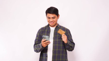 Foto de Hombre asiático adulto sonriendo mientras sostiene la tarjeta de crédito en blanco y el teléfono móvil sobre fondo gris - Imagen libre de derechos