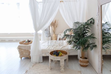 Photo for Daylight through a huge panoramic window illuminates the cozy oriental interior of the room in beige colors with wicker furniture and authentic elements - Royalty Free Image