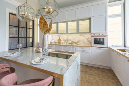 una vista cercana de la elegante cocina blanca con una isla de cocina en el lujoso interior de un apartamento moderno en colores claros con muebles elegantes.