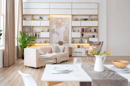 Inneneinrichtung geräumige helle Studio-Wohnung im skandinavischen Stil und warmen Pastellweiß und Beige-Farben. Trendmöbel im Wohnbereich und moderne Details im Küchenbereich.