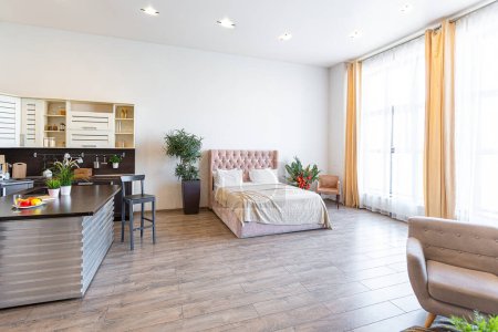 Contemporary ordinary design of spacious studio in soft warm colors. Simple furniture. Light large room with sunlight. Daytime. Tiled brown floor and white walls .