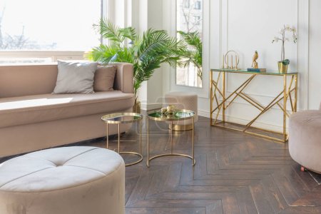 Photo for Very light and bright interior of luxurious cozy living room with chic soft beige furniture with gold metallic elements, huge window to the floor and wooden parquet - Royalty Free Image